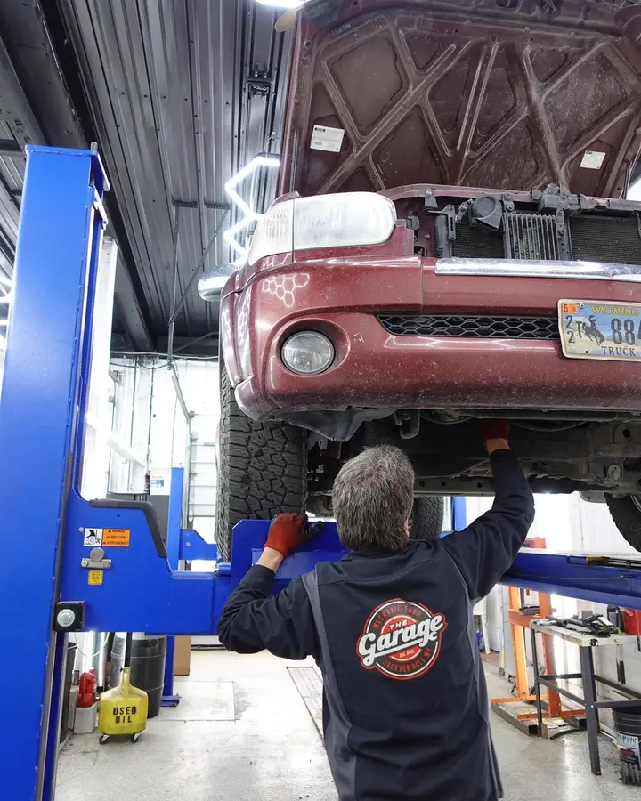 Technician working beneath a lifted SUV inside The Garage service bay